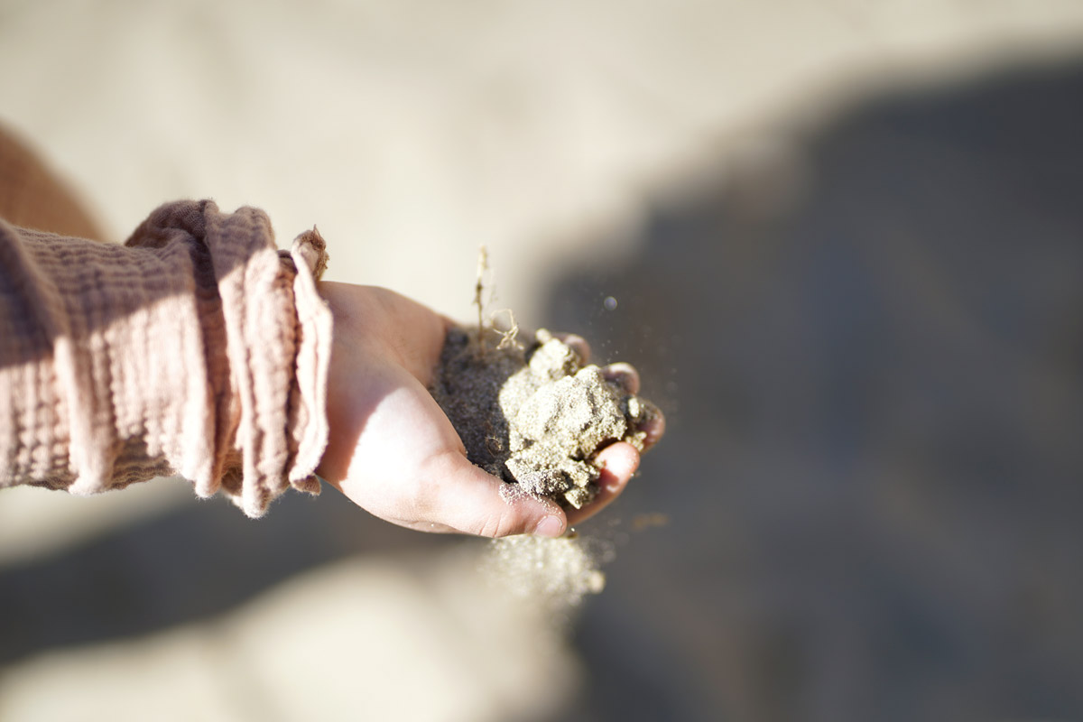 Kind lässt Sand aus der Hand rieseln